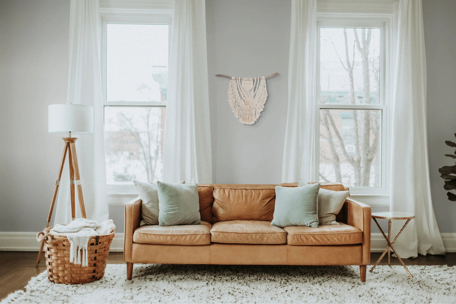 Jolie tenture macramé murale suspendue au mur d'un salon derrière un canapé.