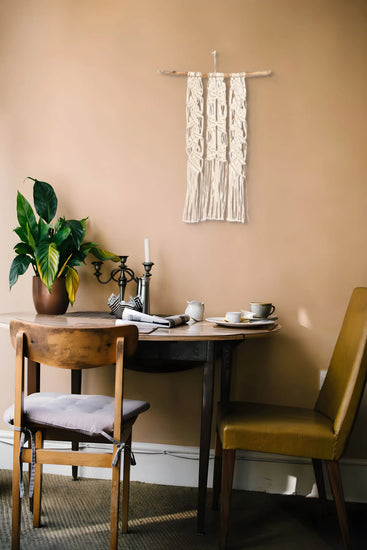 Tenture en macramé Arbre à papillons accrochée au mur derrière une table en bois