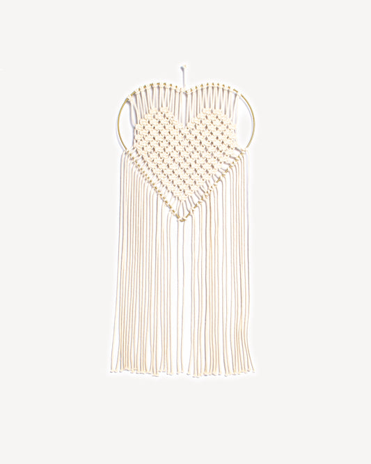 Macramé mural en forme de cœur avec tissage écru et support doré.