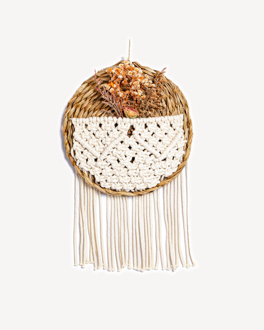 Panier mural rond en osier avec tissage en macramé et bouquet de fleurs séchées.