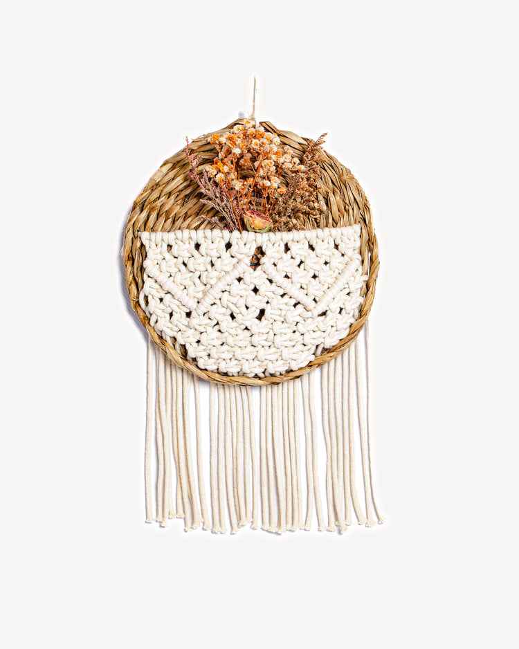 Panier mural rond en osier avec tissage en macramé et bouquet de fleurs séchées.