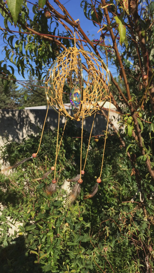 Vidéo du capteur de rêves 3D en corde à macramé en coton safran, suspendu à une branche, tournoyant sous la lumière du soleil. Le prisme diffracte les couleurs, créant un effet lumineux magique.