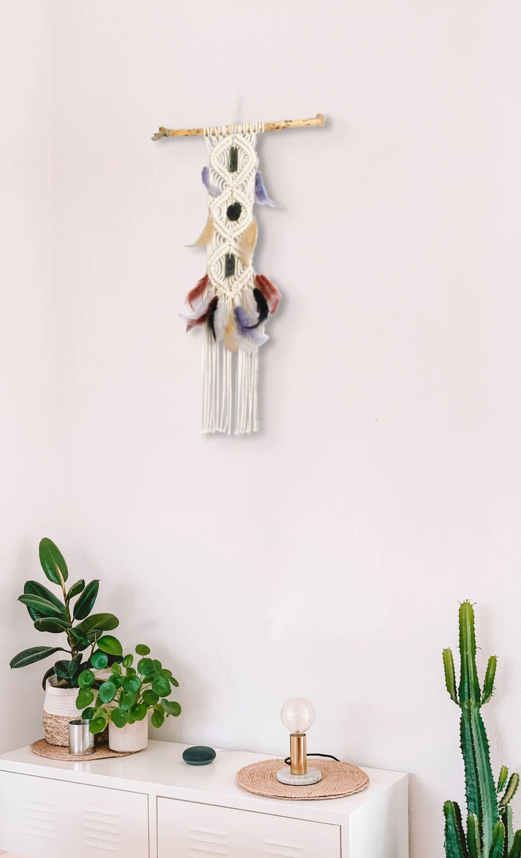 Tenture macramé accrochée au mur au-dessus d'un meuble blanc avec des plantes